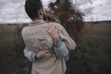 Birbirine aşık bir çift, bulutlu bir havada açık soya fasulyesi tarlasında yürür ve bol bol sarılır.