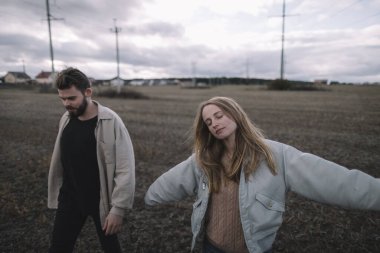Birbirine aşık bir çift, bulutlu bir havada açık soya fasulyesi tarlasında yürür ve bol bol sarılır.
