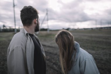Birbirine aşık bir çift, bulutlu bir havada açık soya fasulyesi tarlasında yürür ve bol bol sarılır.