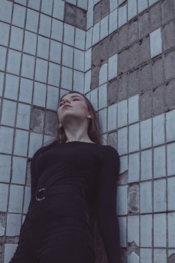 Korkuyla köşeye sıkıştırılan kız duruyor, bakıyor ve ellerini kıvırıyor.