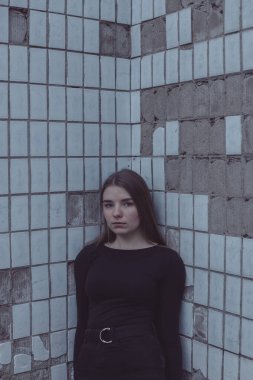 Korkuyla köşeye sıkıştırılan kız duruyor, bakıyor ve ellerini kıvırıyor.