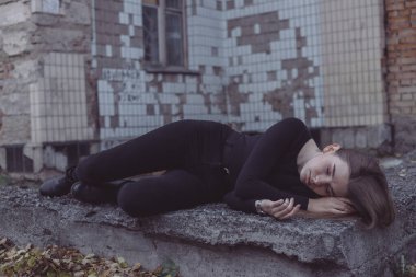 Korkuyla köşeye sıkıştırılan kız duruyor, bakıyor ve ellerini kıvırıyor.