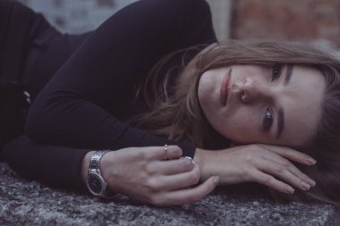 Korkuyla köşeye sıkıştırılan kız duruyor, bakıyor ve ellerini kıvırıyor.