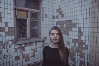 Korkuyla köşeye sıkıştırılan kız duruyor, bakıyor ve ellerini kıvırıyor.