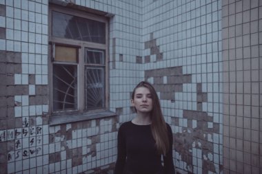 Korkuyla köşeye sıkıştırılan kız duruyor, bakıyor ve ellerini kıvırıyor.