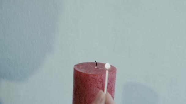 Encender una vela roja de cerca con una sombra en el fondo de una cerilla — Vídeos de Stock