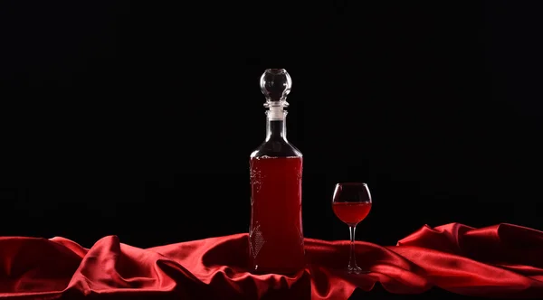 Garrafa e vidro com vinho tinto sobre fundo preto com pano vermelho, tecido de cetim, seda — Fotografia de Stock