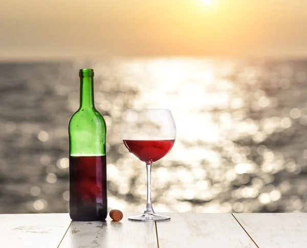 Flaska och glas rödvin på linne bordet mot havet eller havet — Stockfoto