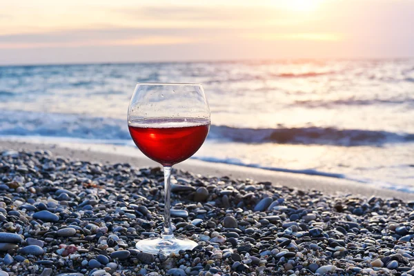 Copo romântico de vinho sentado na praia ao pôr do sol colorido, Copo de vinho tinto contra o pôr do sol, vinho tinto na praia do mar oceano, fundo do céu com nuvens — Fotografia de Stock