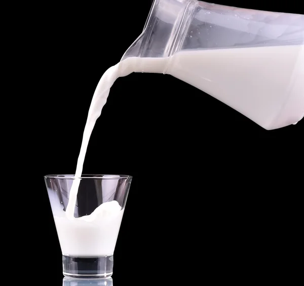 Mleko jest wylewanie z butelki dzbanek do kieliszka na czarnym tle. — Zdjęcie stockowe