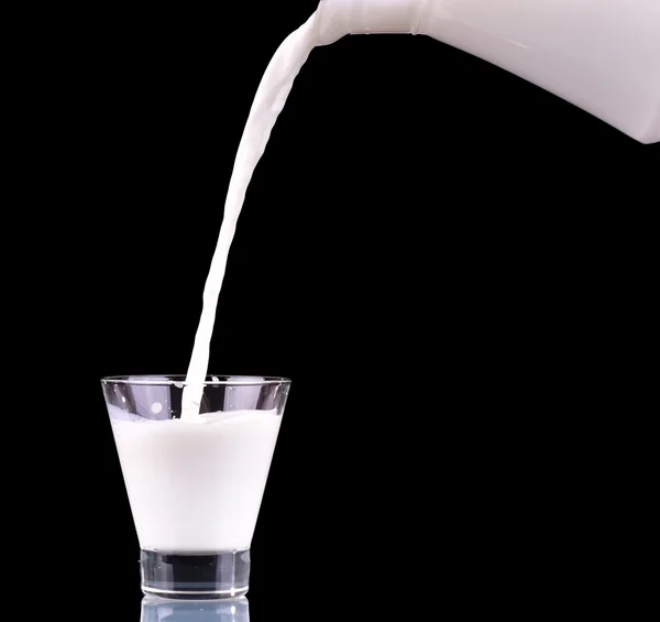 Süt kabı şişeden siyah arka plan üzerine cam içine yağıyor.