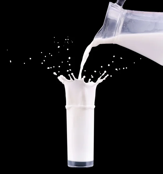 Milch ergießt sich aus der Kanne in das Glas mit Spritzer auf schwarzem Hintergrund. — Stockfoto