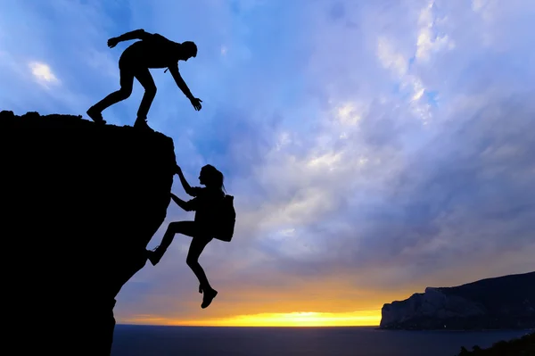 O trabalho em equipe conjunto de duas pessoas homem e menina viajantes ajudar uns aos outros no topo de uma equipe de escalada de montanha, uma bela paisagem pôr do sol . — Fotografia de Stock