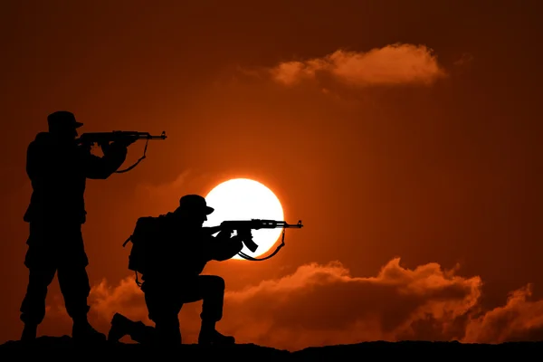 Silhouette militare di due soldati o ufficiali con armi al tramonto. tiro, pistola in mano, cielo colorato, montagna, sfondo, squadra — Foto Stock