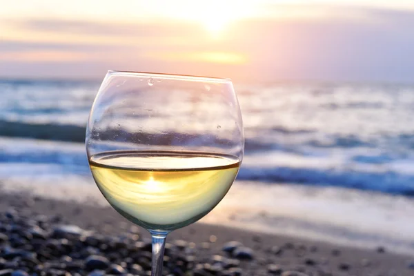 Romantické sklenici vína sedí na pláži barevný západ slunce sklenice bílého vína proti západu slunce, bílé víno na pozadí oblohu s mraky — Stock fotografie