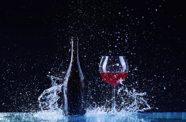 Şişe ve bardak kırmızı şarap, su sıçrama, koyu siyah arka plan, siyah üzerine kırmızı şarap sıçrama şişe ve cam çevresinde büyük sıçrama masada şarap ile