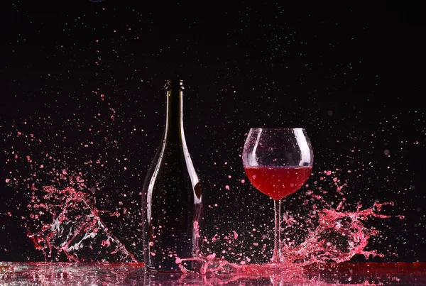 Şarap şişe ve cam ile kırmızı şarap, kırmızı şarap sıçrama, koyu siyah arka plan, siyah üzerine kırmızı şarap sıçrama şişe ve cam çevresinde büyük sıçrama masada dökme