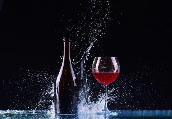 Şişe ve bardak kırmızı şarap, su sıçrama, koyu siyah arka plan, siyah üzerine kırmızı şarap sıçrama şişe ve cam çevresinde büyük sıçrama masada şarap ile