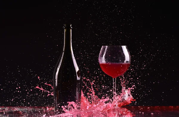 Botella y copa con vino tinto, salpicadura de vino tinto, vino que vierte en la mesa sobre fondo negro oscuro, gran salpicadura alrededor de vidrio y botella de vino tinto salpicadura en negro —  Fotos de Stock