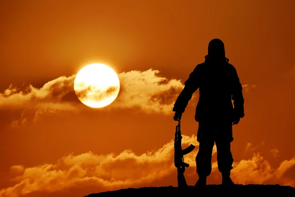 Silhueta de soldado militar ou oficial com armas ao pôr do sol. tiro, segurando arma, céu colorido, montanha, fundo — Fotografia de Stock