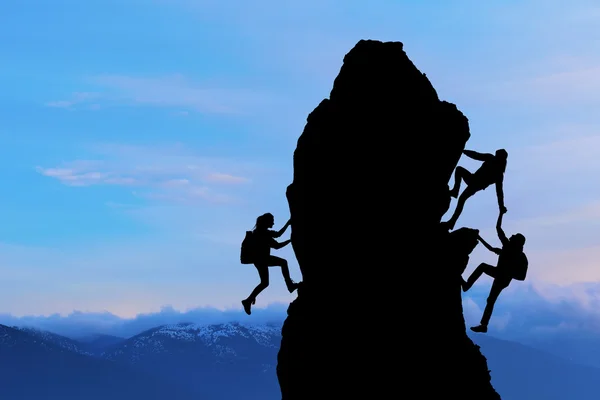Het gezamenlijke werk teamwork van twee mannen reizigers en meisje elkaar helpen op de top van een berg beklimmen team, een mooie zonsondergang landschap — Stockfoto