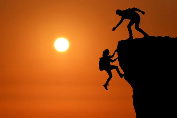 The joint work teamwork of two people man and girl travelers help each other on top of a mountain climbing team, a beautiful sunset landscape. — Stock Photo, Image