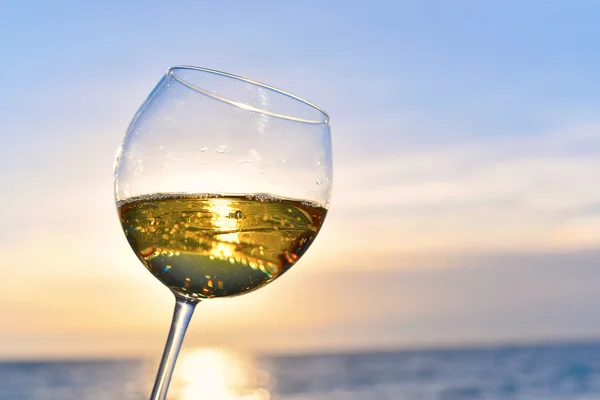 Romantiska glas vin sitter på stranden vid färgstark solnedgång glas vitt vin mot solnedgången, vitt vin på himmel bakgrund med moln — Stockfoto