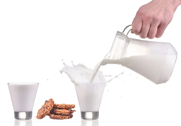 Espirro derramando de um leite de garrafa em vidro e biscoitos isolados em branco Fotografia De Stock