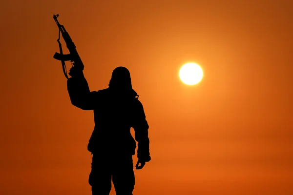 Silueta de soldado militar o oficial con armas al atardecer. disparo, pistola de mano, cielo colorido, montaña, fondo Imagen de archivo