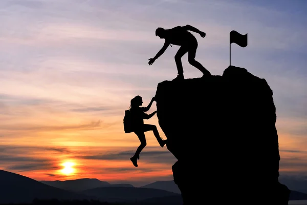 The joint work teamwork of two people man and girl travelers help each other on top of a mountain climbing team, a beautiful sunset landscape. — Stock Photo, Image