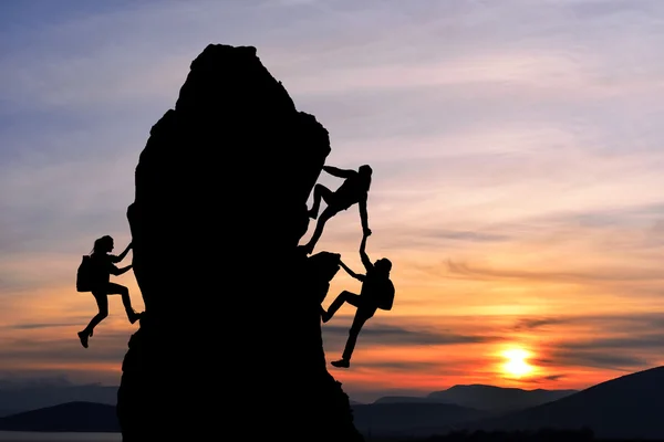 El trabajo conjunto en equipo de dos hombres viajeros y una chica se ayudan mutuamente en la parte superior de un equipo de escalada, un hermoso paisaje al atardecer — Foto de Stock