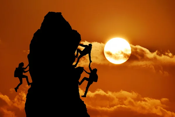 Совместная работа двух мужчин-путешественников и девушки помогают друг другу на вершине альпинистской команды, красивый пейзаж заката — стоковое фото