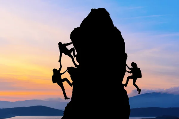 Het gezamenlijke werk teamwork van twee mannen reizigers en meisje elkaar helpen op de top van een berg beklimmen team, een mooie zonsondergang landschap — Stockfoto