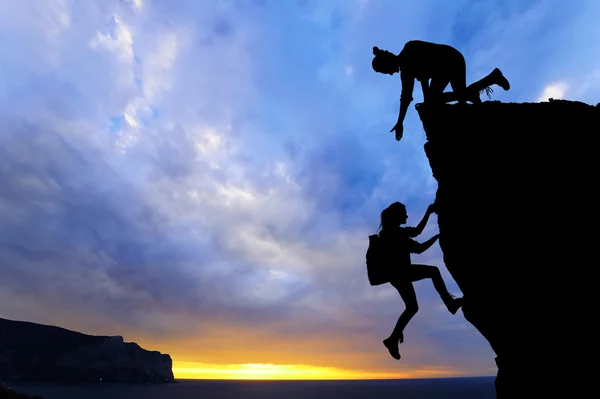 Het gezamenlijke werk teamwork van twee mensen man en meisje reizigers elkaar helpen op de top van een berg beklimmen team, een mooie zonsondergang landschap. — Stockfoto