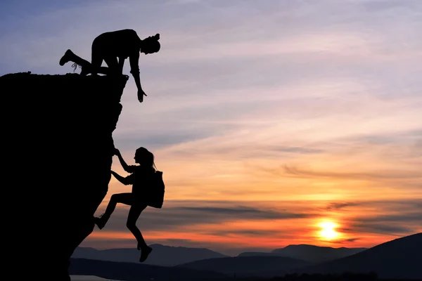 The joint work teamwork of two people man and girl travelers help each other on top of a mountain climbing team, a beautiful sunset landscape. — Stock Photo, Image