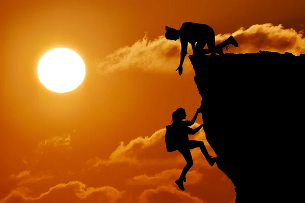 Het gezamenlijke werk teamwork van twee mensen man en meisje reizigers elkaar helpen op de top van een berg beklimmen team, een mooie zonsondergang landschap. — Stockfoto