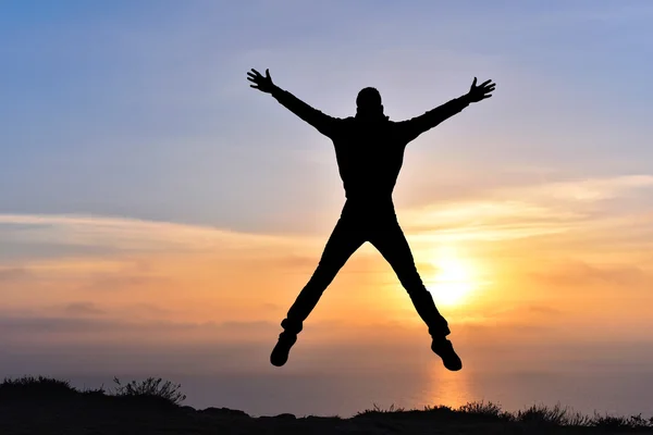 Silueta de hombre feliz en la puesta del sol en la roca de la montaña sobre el mar —  Fotos de Stock