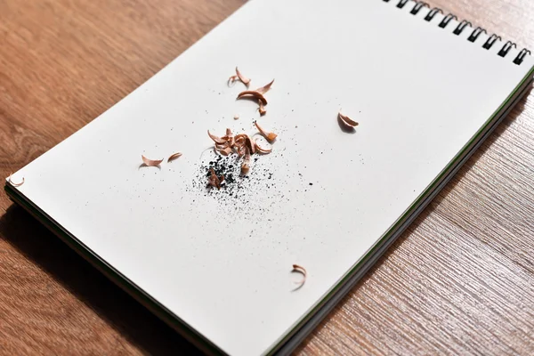 Open notebook with pencil shavings on wooden table — Stock Photo, Image
