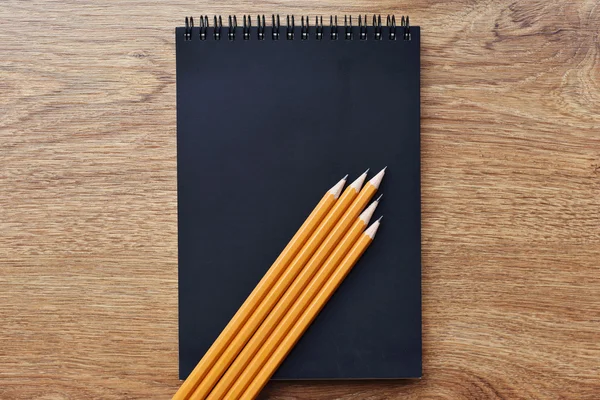 Black blank notebook on grunge wood background with yellow pencils — Stock Photo, Image