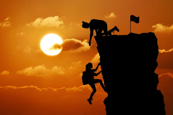 The joint work teamwork of two people man and girl travelers help each other on top of a mountain climbing team, a beautiful sunset landscape. — Stock Photo, Image