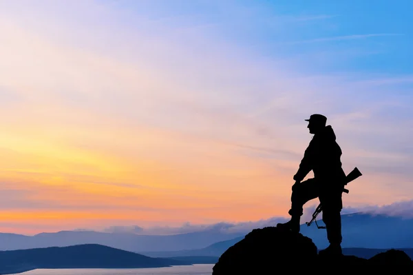 Silhuett av militär soldat eller officer med vapen vid solnedgången. skott, hålla pistolen, färgglada himmel, berg, bakgrund Stockfoto