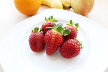 Five strawberries with peduncles in the middle of a white plate clipart