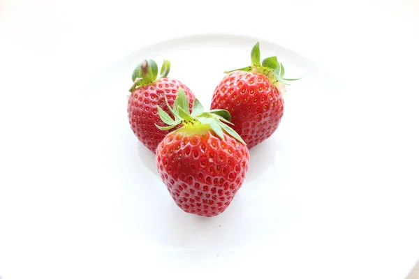 Three strawberries with peduncles in the middle of a white plate — Stock Photo, Image