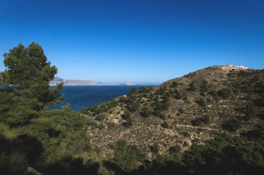 Arka planda doğal parkın güneşli panoramik manzarası 'Serra Gelada' deniz feneri ve Calpe Rock 'Ifach' ı, Albir, Costa Blanca, İspanya