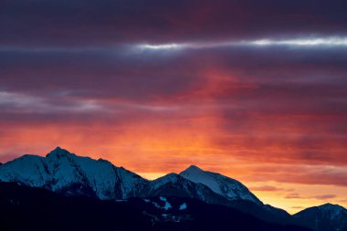 Rocky alpine mountain range during sunset with red orange illuminated clouds in Tirol, Austria