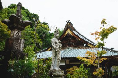 Miyajima, Hiroşima, Japonya 'daki Daisho-in Tapınağı' ndaki tapınaklar ve sonbahar renkli ağaçlar arasındaki Budist heykeli.