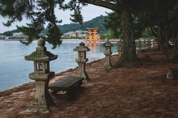 在常青树下的长椅公园 俯瞰着日本广岛宫岛市海洋湾中漂浮的鸟里门 — 图库照片