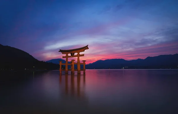 Itsukushima Tapınağı 'nın yüzen Torii Kapısı alacakaranlıkta gün batımından sonra Miyajima, Hiroşima, Japonya' da kırmızı renkli bulutlar ile