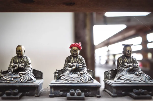 Small bronze buddhist statues with coin and hat offerings, which are believed to make worshippers dreams come true in Daisho-in temple in Miyajima, Hiroshima, Japan
