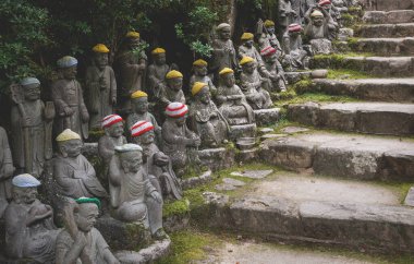 Buda heykelleri, merdivenler boyunca örülmüş renkli şapka adakları ile tarihi Buda Shakyamuni 'nin ilk 500 havarisini temsil ediyor Miyajima, Hiroşima, Japonya' daki Diasho-in tapınağında.